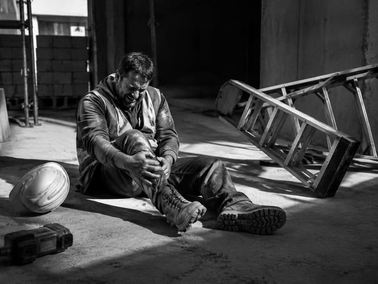 Worker on the ground holding his leg beside a fallen ladder